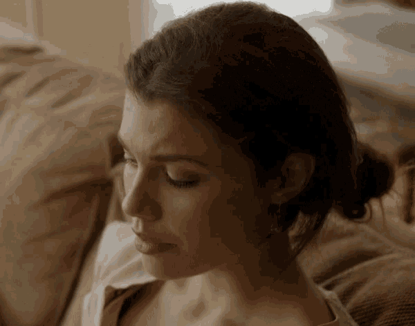 a woman sitting on a couch with her eyes closed and her hair in a bun