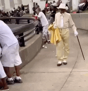 an elderly man is walking down a sidewalk with a cane and a yellow jacket .
