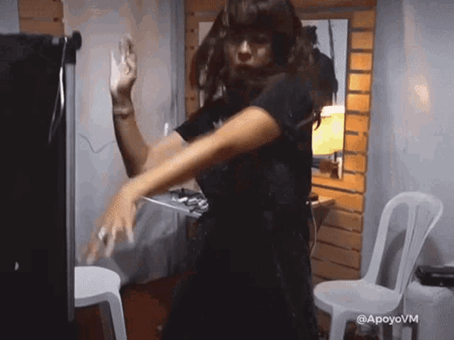 a woman in a black dress is dancing in a room with chairs and a sign that says apoyo vm
