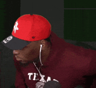 a man wearing a red hat and a maroon texas sweatshirt is listening to music with headphones .