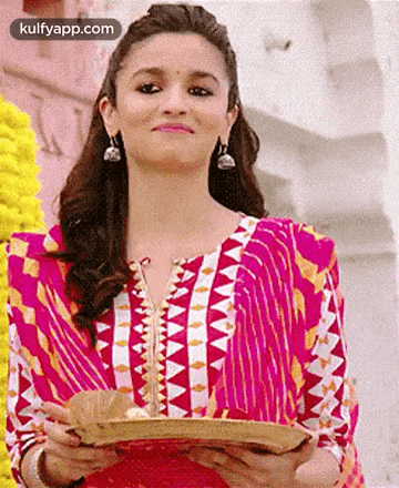 a woman in a pink dress is holding a tray in her hands and smiling .