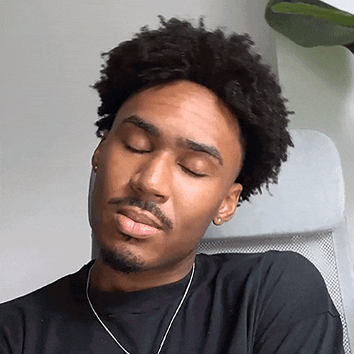 a man with curly hair and a beard is sitting in a chair with his eyes closed .