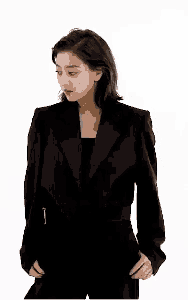 a woman is wearing a black suit and standing with her hands in her pockets .