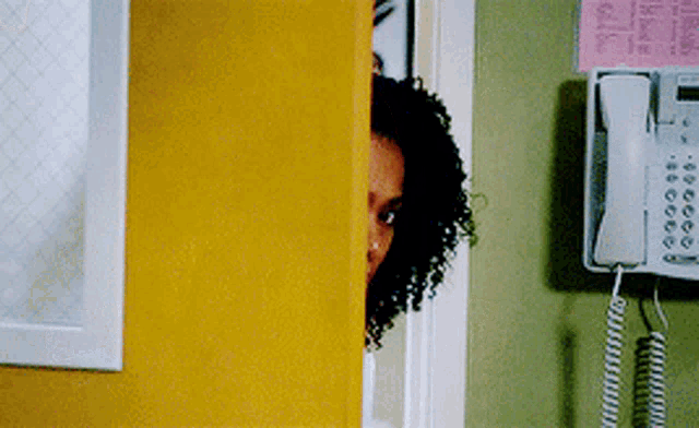 a woman peeking out from behind a yellow door