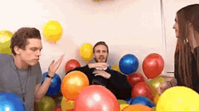 a group of people are sitting in a pile of balloons .