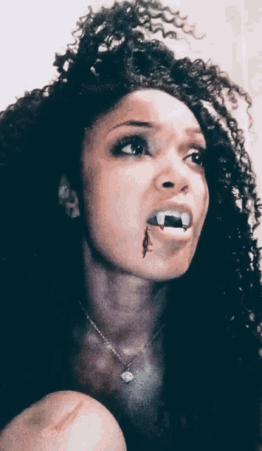 a woman with vampire teeth in her mouth has a necklace around her neck
