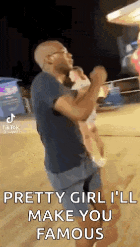 a man is holding a baby in his arms and says `` pretty girl , i 'll make you famous '' .
