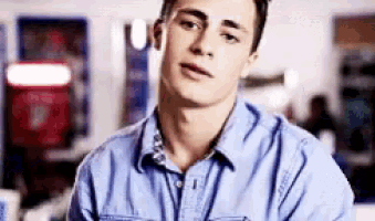 a young man wearing a blue denim shirt is looking at the camera