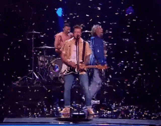 a man is singing into a microphone while playing a guitar on a stage with confetti falling around him .