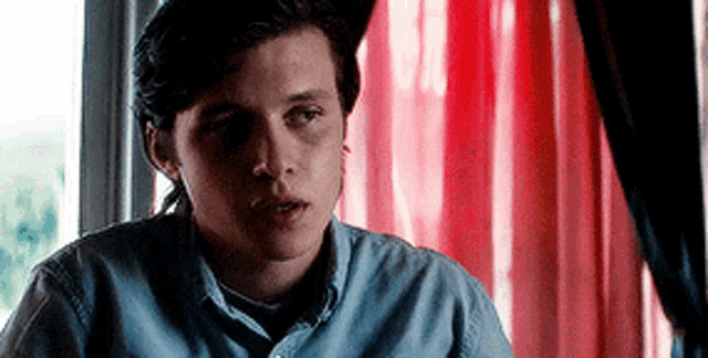 a young man in a blue shirt is sitting at a table in front of a red and white striped curtain .