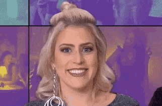 a woman is smiling in front of a purple background while wearing a necklace and earrings .