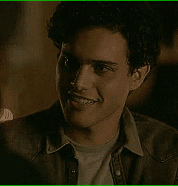 a young man with curly hair is smiling for the camera .