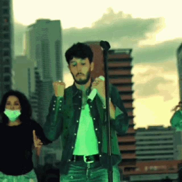 a man singing into a microphone while a woman wearing a mask stands behind him