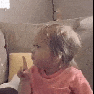 a little girl in a pink shirt is sitting on a couch making a face .