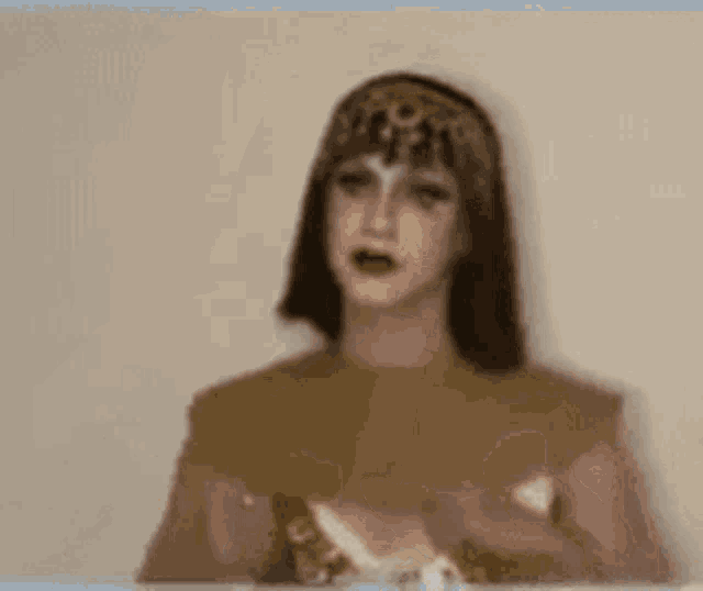 a woman in a costume with a crown on her head is standing in front of a wall .