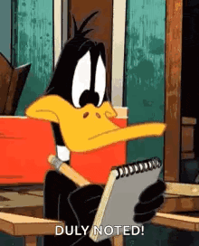 daffy duck is sitting at a table holding a notebook and a pen .