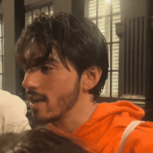 a man with a beard is wearing an orange sweatshirt