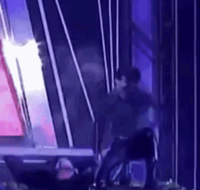 a man in a black shirt is standing on a stage in front of a purple wall .