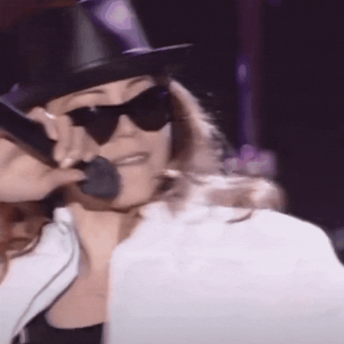 a woman wearing sunglasses and a top hat is singing into a microphone