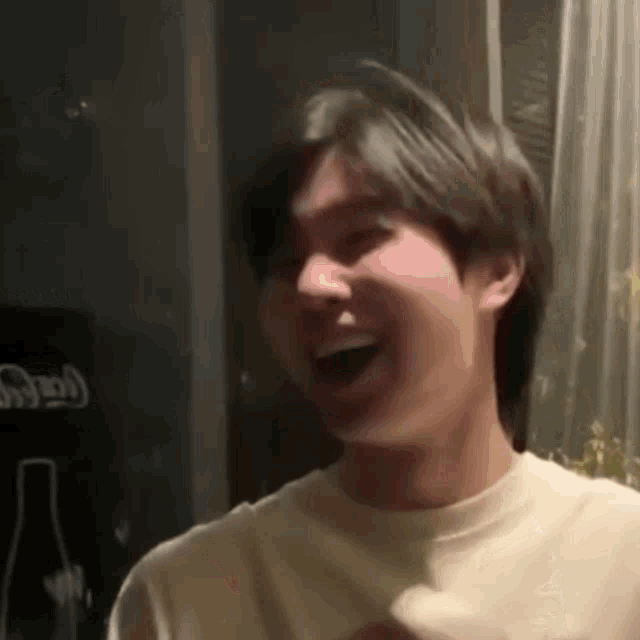 a young man is laughing while sitting in front of a coca cola bottle .