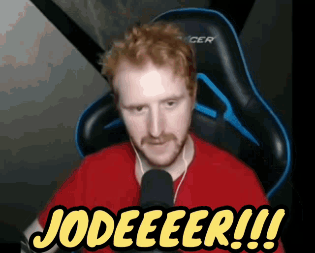 a man in a red shirt is sitting in front of a microphone and says jodeeeer