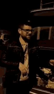 a man in a black jacket is standing next to a car at night .