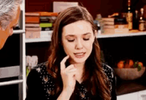 a woman sitting in front of a bookshelf with a man in the background