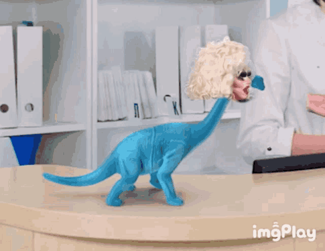 a blue dinosaur with a drag queen 's head on its neck