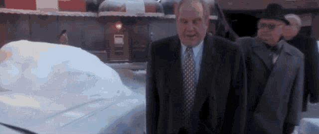 a man in a suit and tie is standing in front of a large pile of snow .