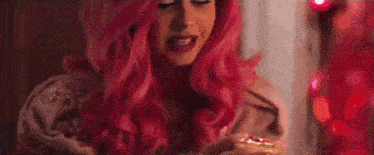 the woman is wearing a pink wig and holding a red object .