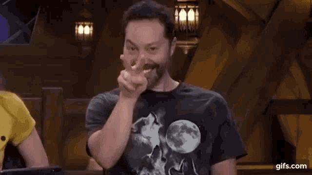 a man with a beard is pointing at the camera while wearing a black t-shirt with a wolf on it .