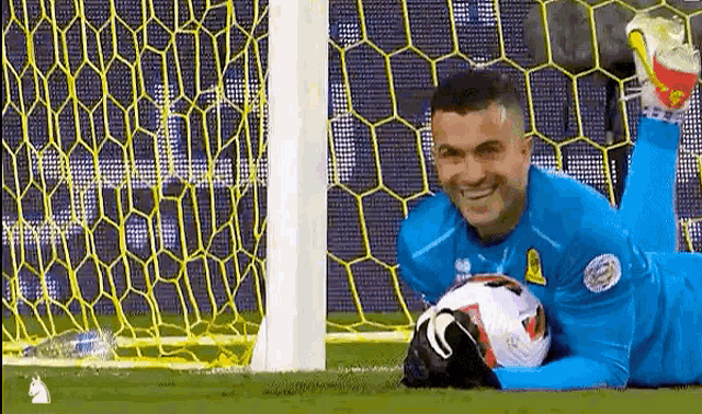 a soccer goalie is laying on the field with a soccer ball in his hands .