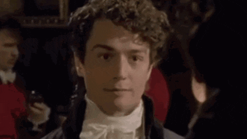 a man with curly hair is wearing a tuxedo and tie and looking at the camera .