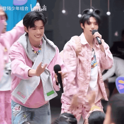a man in a pink jacket is singing into a microphone while another man stands behind him
