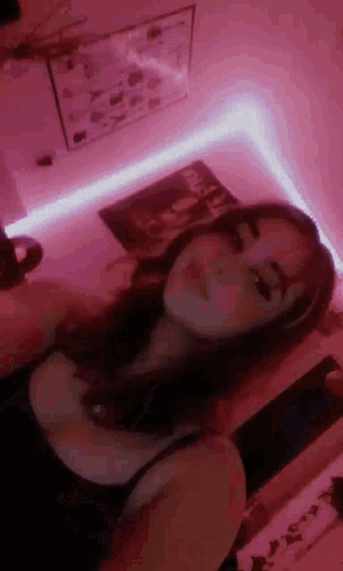 a woman is taking a selfie in a room with pink lights on the walls .