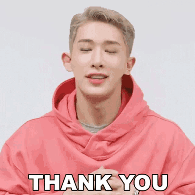 a man in a pink hoodie is saying thank you with his eyes closed