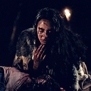 a woman with blood on her face is holding a dead man in a dark room