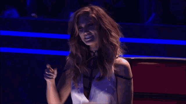 a woman in a white dress is smiling and pointing at the camera