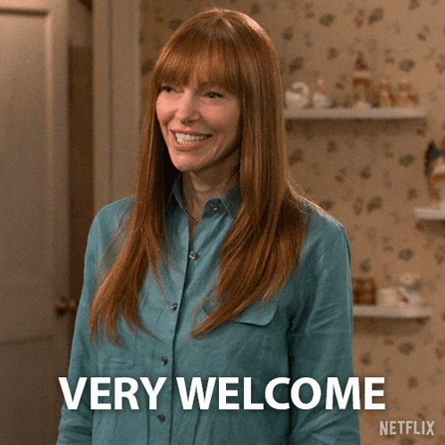 a woman in a blue shirt says " very welcome " while waving