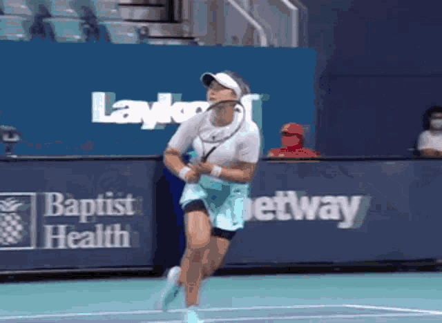 a woman is playing tennis on a court with a baptist health banner in the background