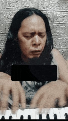 a man with long hair is playing a piano with a black rectangle covering his face