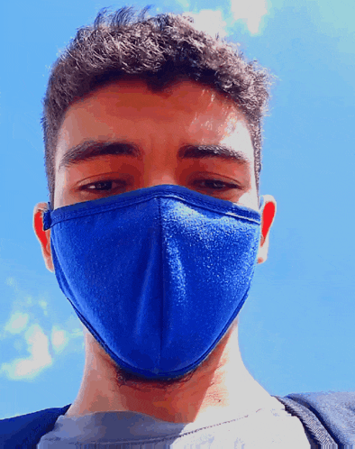 a young man wearing a blue face mask looks at the camera