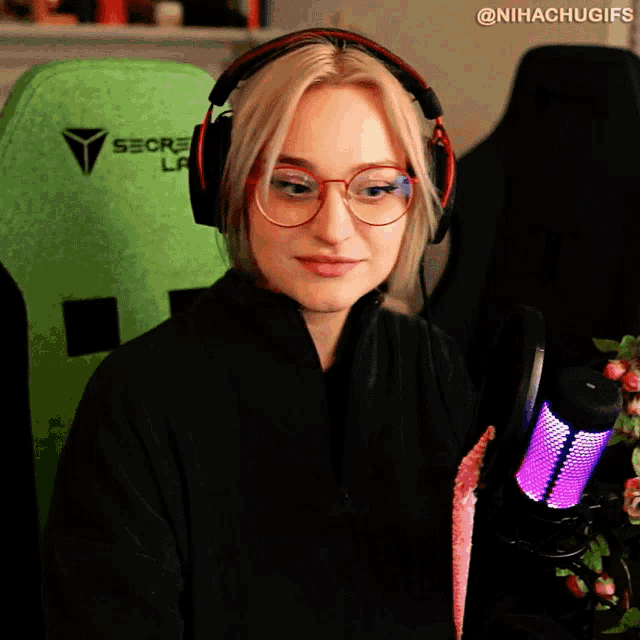 a woman wearing glasses and headphones is sitting in front of a green secret lab chair