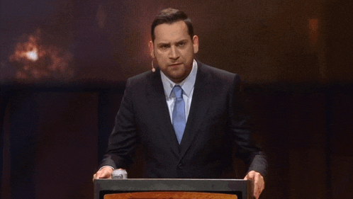 a man in a suit and tie stands behind a podium giving a speech
