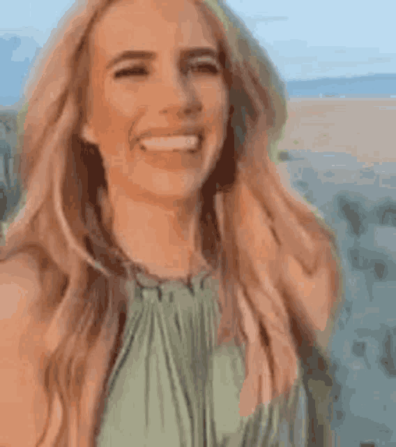 a woman in a green dress is smiling and laughing while standing on a beach .