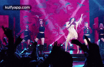 a woman is singing into a microphone while dancing on a stage in front of a crowd .