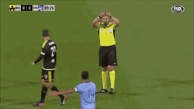 a referee is standing on a soccer field with his arms outstretched and a fox sports logo in the corner .