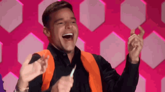 a man wearing a black shirt and an orange vest laughs with his hands in the air