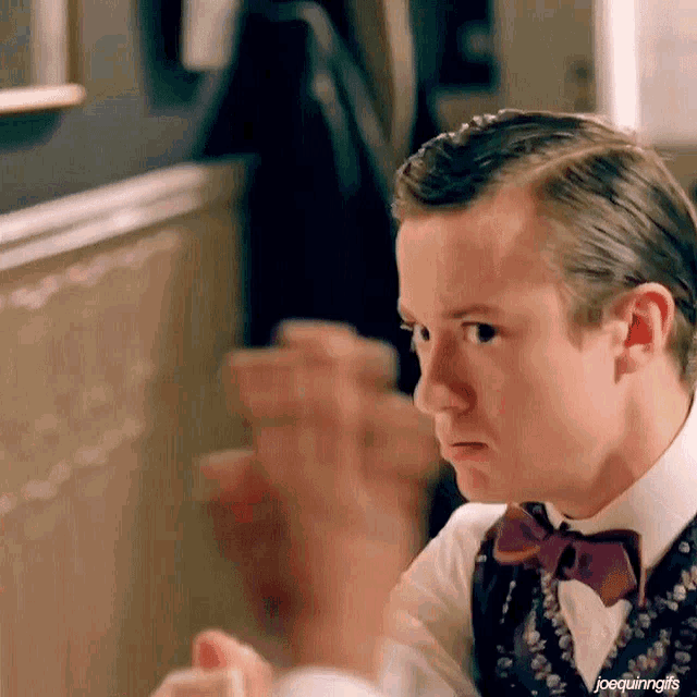 a man wearing a bow tie and a vest is sitting at a table looking at something .