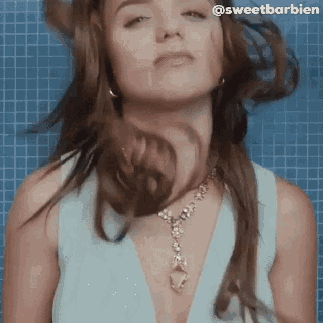 a woman in a blue dress and necklace is standing in front of a blue tile wall .